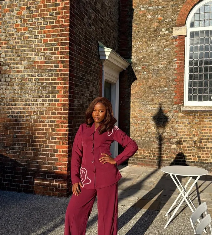 Precious standing in a burgundy suit beside a brick building
