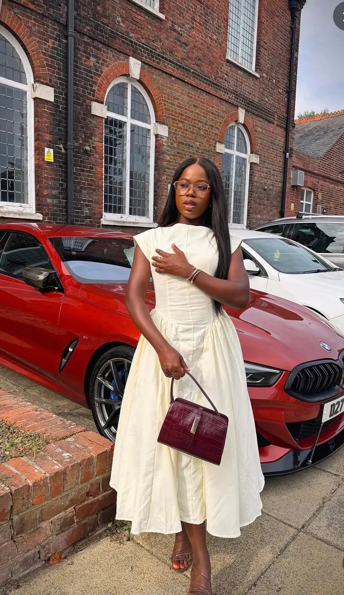 Precious in an ivory dress beside a red car